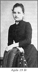 Foto av Agda Östlund vid 19 års ålder. Hon står lutad mot en karmstol och har en höghalsad  svart klänning på sig.