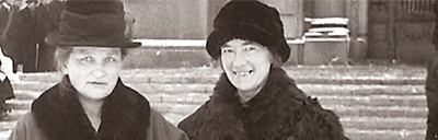 Foto av Agda Östlund och Nelly Thüring utanför riksdagen 1922. Båda har hatt och kappa.