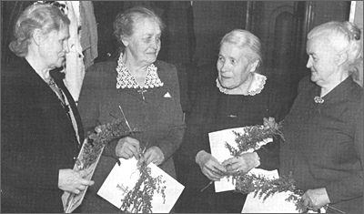 Foto av fyra äldre kvinnor med blommor och papper i händerna står och samtalar