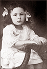 Foto av Durriya som barn, sittande på en stol med rosetter i håret. Hon ser allvarlig ut