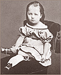 Foto av en liten flicka som sitter på en gammaldags finstol med tofs