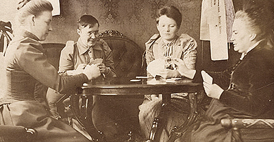 Foto av Minna Canth och tre andra som spelar kort i en salong med gammaldags bord