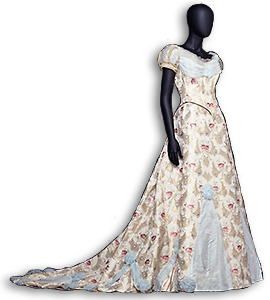 Foto av docka iförd en klänning med släp. Tyget går i blekgult med guldinslag och rosa blommor. Infälla delar av ljusblå siden, släp och puffärmar. 