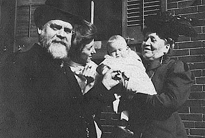 Foto av Tinius i hög hatt, Charlotte i stilig hatt med tillbehör och dottern. Charlotte håller barnbarnet i famnen.