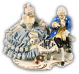 En kvinna och en man spelar schack i en målad porslinsgrupp med spets till kläderna.