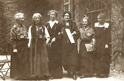 Foto av sex kvinnor som står på rad ute på en gård, flera av dem håller varandra under armarna