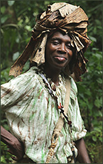 Färgfoto av svart kvinna med stor sjal över huvudet. I bakgrunden anas djungeln.