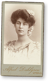Visitkortsfoto av Elin Henriques som ung. Hon har håret uppsatt med rosetter som hänger bak och en ljus klädning på sig. Nederst på bilden står fotografens namn: Alfred Dahlgren, Uppsala