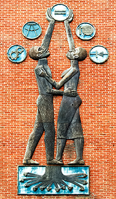 Väggskulptur av en man och en kvinna som sträcker sig mot fem olika symboler ovanför dem, mot en tegelvägg