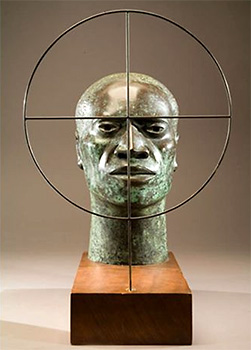 Skulptur av manshuvud med ett träffkors framför