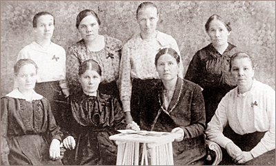 Foto av åtta kvinnor, hälften står, hälften sitter med ett litet bord framför sig