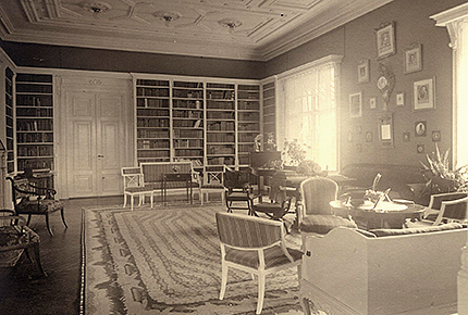 Interiörbild från biblioteket med högst i tak och tjusiga dörrar, böcker i bokhyllor infällda i väggen, många sittgrupper och en tavelvägg