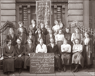 Foto av tre rader av kvinnor som sitter i en trappa. Längst bak är ett standar med texten Irish Women Workers Union och längst fram finns ett plakat med rubriken "Freedom's Martyrs"