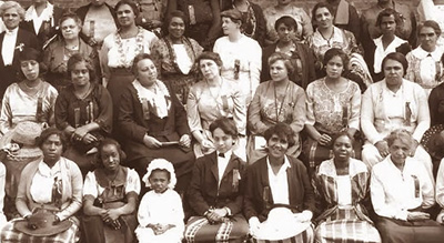 Beskuret foto av många kvinnor och något litet barn som sitter och står i tre-fyra rader bakom varandra
