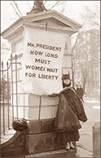Foto av kvinna som står i regnväder med ett stort standar med texten: Mr President, how long must women wait for liberty