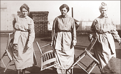 Foto av tre kvinnor i fängelsekläder. Alla bär på varsin stol utomhus