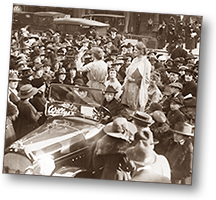 Foto av två kvinnor som står upp i en stillstående bil. Kvinnan till vänster talar. Massor av folk är samlade omkring dem och lyssnar. I bakgrunden syns några bilar längre bort