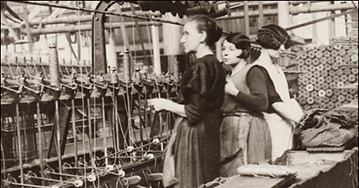 Foto av tre kvinnor, en äldre och två yngre, i en fabrikslokal
