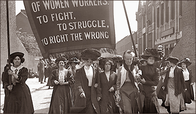Foto av kvinnor i en demonstration, där de i täten bär en banderoll och det som syns av texten är: "...of Women Workers to fight, to struggle, to right the wrong"