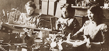 Foto av tre kvinnor som sitter och arbetar med att tillverka träleksaker
