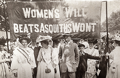 Foto av ett demontrationståg med två kvinnor och en man i spetsen framför en stor banderoll