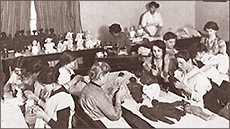 Foto på kvinnor som sitter runt bord och tillverkar dockor i WFL:s leksaksfabrik