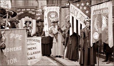 Foto av ett antal kvinnor som står på en gata omringade av standar