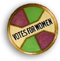 Röckmärke i vitt, lila, grönt och guld, med svart text: Votes for women, i mitten