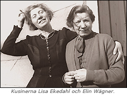 Foto av kusinerna Lisa Ekedahl och Elin Wägner, som står utomhus, kanske på en balkong, det syns att det blåser i håret på dem. Lisa har armen om Elin.