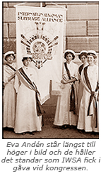 Foto av fem studentmarskalker i helfigur. De håller upp ett standar . Under bilden står: Eva Andén står längst till höger i bild och de håller det standar som IWSA fick i gåva vid kongressen