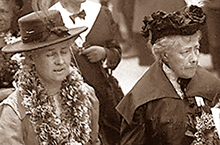 Närbild av Gulli Petrini och Frigga Carlberg i ett demonstrationståg. De har hattar på huvudena, Frigga ser åt sidan, medan Gulli blundar