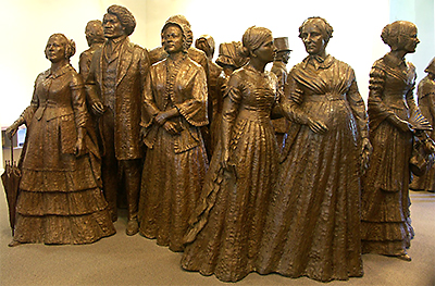 Färgfoto av en stor brosstaty föreställande en stor grupp kvinnor och en man, Frederick Douglass. Kvinnorna har långa klänningar och en håller i ett paraply, de står vända åt olika håll, så att gruppen kan ses från flera vinklar