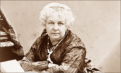 Foto av Elizabeth Cady Stanton sittande och lutande sig mot ett bord som inte syns i bild. Hon ser rakt i i kameran