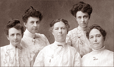 Foto av fem kvinnor i fina spetsblusar och med uppsatt hår. Alla ser in i kameran och några ler