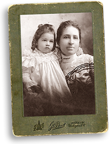 Foto av Mary i halvfigur med dottern Phyllis i famnen. Båda är klädda i fina kläder med spetsar
