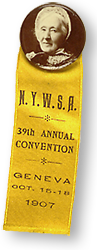 Deltagarmärke i form av en rund bild av Elizabeth Smith Miller och ett gult band. På bandet står: N.Y.W.S.A. 39th Annual Convention - Geneva - oct. 15-18 1907