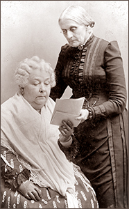 Foto av Elixabeth Cady Stanton som sitter och håller upp några papper, medan Susan B. Anthony står bredvid och också håller i pappren,. Det syns att de är gamla
