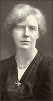 Porträttfoto av lite äldre Mary Macarthur med uppsatt hår, en brosch i form av en fågel och ett pärlhalsband