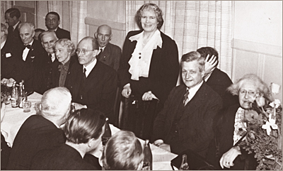 Foto av ett antal män och några kvinnor runt ett bord. En kvinna står upp och ser in i kameran. Lydia Wahström syns halvt skymd i nedre högra hörnet