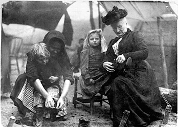 Foto av Mother Jones och en annan kvinna som sätter på skor på två fattigt klädda barn