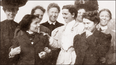 Foto av åtta kvinnor i halvfigurm de ser glada ut, flera skrattar. Näst längst till höger står Agnes Nestor, som håller hakan i handen och ser lite fundersam, men leende, ut.