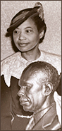Foto av Augusta Savages iförd hatt stående bakom ett av hennes porträttverk