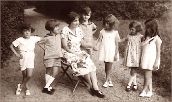 Foto av en kvinna som sitter på en enkel stol, omgiven av sex barn i förskoleålder tomhus