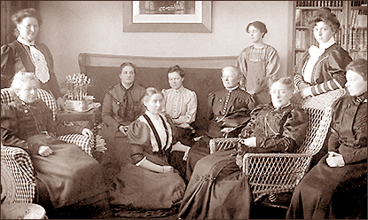 Foto av ett antal kvinnor i ett vardagsrum med soffa och korgstolar. I bakgrunden skymtar en tavla på väggen och en bokhylla till höger