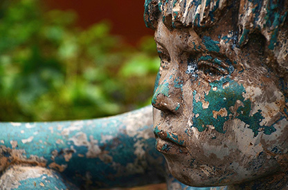 Starkt beskuret foto av en ärgad staty föreställande en pojkes ansikte och bit av en arm