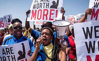 Foto av strejkande arbetare, i mitten en kvinna som ropar i en megafon