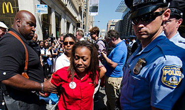 En ung tjej grips av en civilklädd man medan några poliser tittar på.