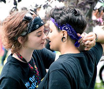 Foto av två unga tjejer på väg att kyssa varandra. Båda har bandanas vid håret, den enda har solglasögon uppsatta på håret