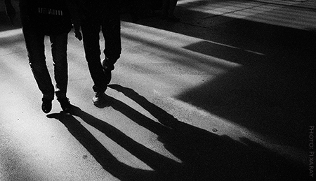 Photo of the legs of two men walking towards their own shadows