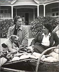 Foto av Victoria och Maria Rosa sittande i en trädgård utanför ett hus, en hund har hoppat upp på solstolen Maria Rosa sitter i